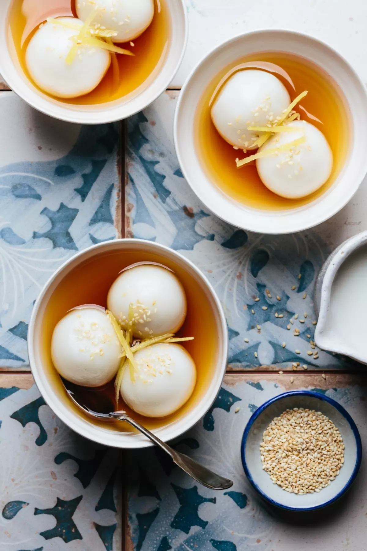 Three bowls of Vietnamese glutinous rice balls in a warm ginger syrup with a cup of coconut sauce and a bowl of toasted sesame seeds
